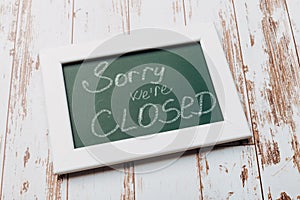 Sign `Sorry, we are closed` on a chalk board with English inscriptions on a wooden background. Closed business