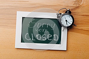 Sign `Sorry, we are closed` on a chalk board with English inscriptions on a wooden background. Closed business