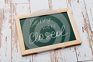 Sign `Sorry, we are closed` on a chalk board with English inscriptions on a wooden background. Closed business