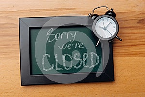 Sign `Sorry, we are closed` on a chalk board with English inscriptions on a wooden background. Closed business