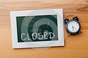 Sign `Sorry, we are closed` on a chalk board with English inscriptions on a wooden background. Closed business