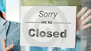 Sign Sorry we re closed on shop entrance door as new normal shutdown. Woman in mask gloves hangs closed sign on front door of cafe