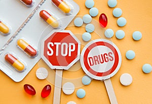 Sign Stop drugs. Colorful pile of medicines and painkillers on yellow background