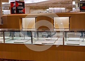 Sign for a store closing sale on top of an empty jewelry display case with empty illuminated shelves.