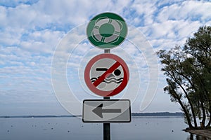 Sign with a swimming ring, red sign with a crossed out swimmer and white sign with an arrow pointing to the left at the lake beach