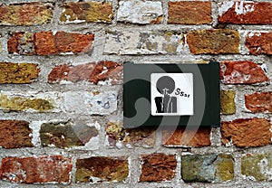 Sign/symbol of request for silence/mute on brick wall in Bruges/Brugge, Belgium