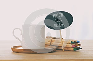 sign with text: FOLLOW YOUR DREAMS next to cup of coffee over wooden table.