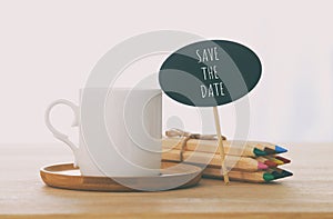 sign with text: SAVE THE DATE next to cup of coffee over wooden table.