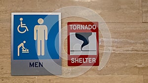 Sign of a tornado shelter next to a sign of a men`s restroom