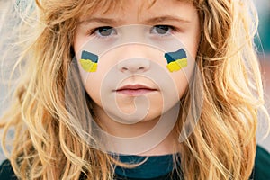 Sign of ukrainian flag on child cheek. Ukrainian geopolitics globe crisis. Close up kids face.