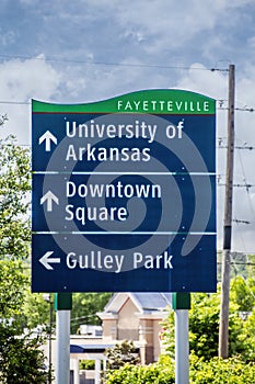 Sign for University of Arkansas and downtown Square and Gulley Park with blurred background of trees and buildings