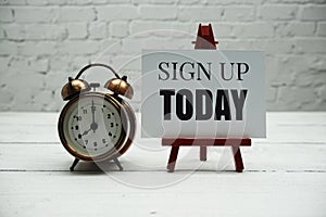 Sign up Today text and alarm clock on white brick wall and wooden background