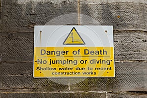 A sign on a wall near the sea warning of the dangers of jumping in the sea and that there is a danger of death