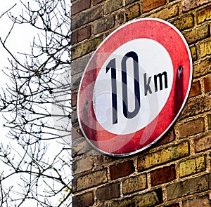 Sign on a wall with yellow bricks indicating the maximum applicable speed of 10 kilometres per hour