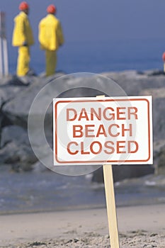 A sign warning, dangerï¿½beach closed with cleanup crews in the background