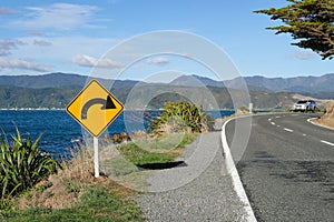 Sign warning of a upcoming bend on an ocean road