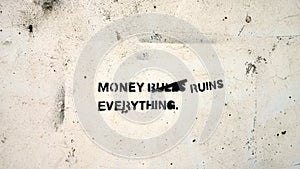 Sign on a White Wall stating Money Rules Everything changed to Money Ruins Everything