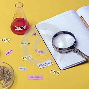 signature with the name of the food additive under a magnifying glass on a table with flasks and a notebook. Unhealthy