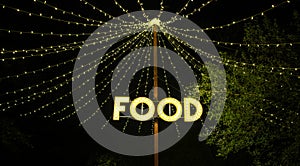 Signboard with word food made with light bulbs hung on wooden post under light garlands photo