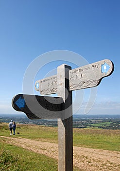 A signpost and a couple walking with a dog on the South Downs Way near Brighton in Sussex, England, UK