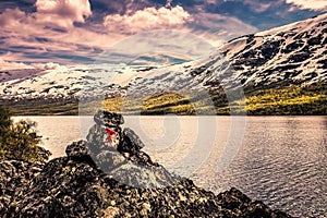 Signpost for Trail in front of a lake and snowy mountains in Norway