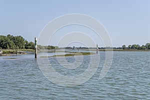 signposts draw a canal among saltmarshes at lagoon, Grado, Friuli, Italy