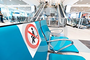 Signs on the seats at the airport draw line between safe and dangerous areas for Seating to comply with safe social distance.