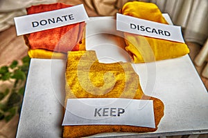 Signs with the words keep, donate, discard and fashion clothes folded in stacks in cozy room. The concept of cluttering