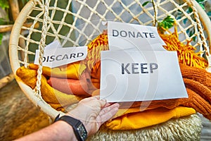 Signs with the words keep, donate, discard and fashion clothes folded in stacks in cozy room. The concept of cluttering