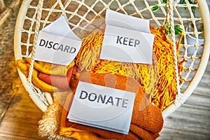 Signs with the words keep, donate, discard and fashion clothes folded in stacks in cozy room. The concept of cluttering