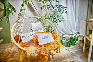 Signs with the words keep, donate, discard and fashion clothes folded in stacks in cozy room. The concept of cluttering