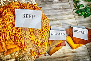 Signs with the words keep, donate, discard and fashion clothes folded in stacks in cozy room. The concept of cluttering