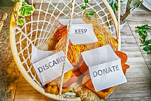 Signs with the words keep, donate, discard and fashion clothes folded in stacks in cozy room. The concept of cluttering