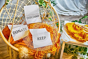 Signs with the words keep, donate, discard and fashion clothes folded in stacks in cozy room. The concept of cluttering