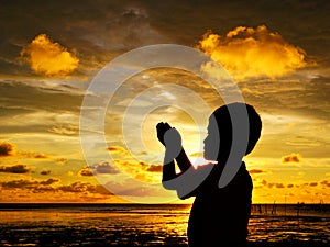 Sihlouette of praying kid during sunset