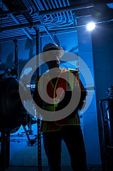 Sihouette of industrial scene lit blue with worker around pipes ,gauges and valves.