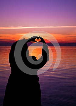 Sihouette of woman making the Heart sign with her hands, against