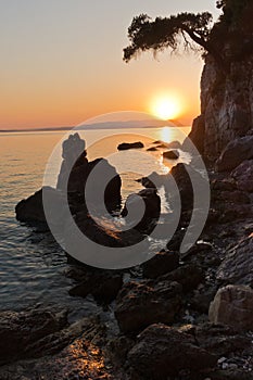 Sihouette of a young couple sitting on a rock at sunset, Kastani Mamma Mia beach, island of Skopelos