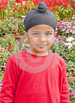 A Sikh boy standing ahead of flowers