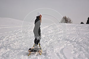 A girl pulls the sled to the top of the snowy mountain photo