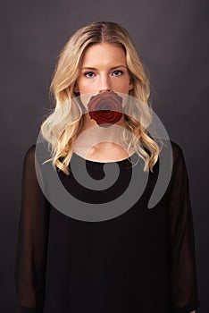 Silenced by love. Conceptual image of a blonde woman with a rose covering her mouth.