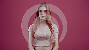 Silent, quiet 20-year-old redhead in a pink casual T-shirt, isolated on a pink background. The concept of people's