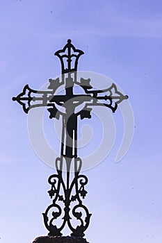silhouete of a decrative, iron cross, on top of, a christian gravestone