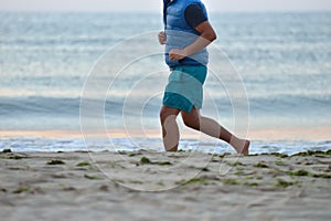 Silhouette of active adult man running and exercising on the beach early in the morning, at the sunrise. Calm water. Healthy life