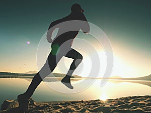 Silhouette of active athlete runner running on sunrise shore. Morning healthy lifestyle exercise