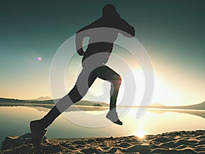 Silhouette of active athlete runner running on sunrise shore. Morning healthy lifestyle exercise