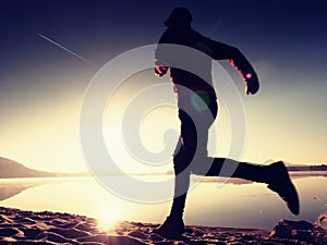 Silhouette of active athlete runner running on sunrise shore. Morning healthy lifestyle exercise