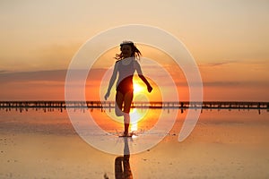 Silhouette of active little child girl in swimsuit is having fun runs and plays on a beach at sunset on summer travel