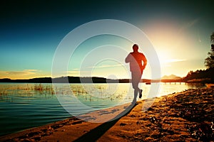 Silhouette of active man running and exercising on the beach at sunset.