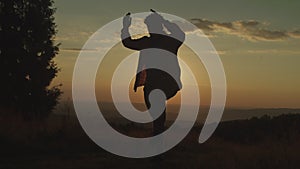 Silhouette of active man standing in balancing, karate kid yoga pose on mountain top at sunset